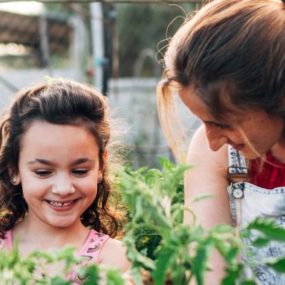une-mère-et-sa-fille-regardent-des-plantes-au-jaridn-en-souriant